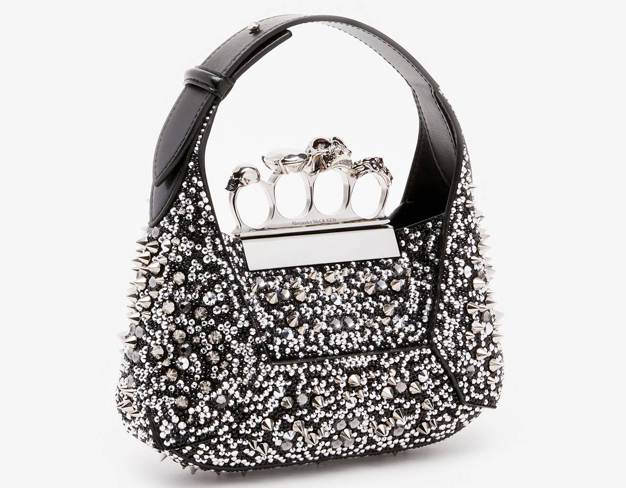 Le sac The Jewelled Hobo, fabriqué en cuir de veau noir, présente une décoration intégrale de clous et de cristaux, ainsi qu'une poignée en finition argent antique avec des anneaux incrustés de cristaux Swarovski. Inspirée d'une pierre facettée reposant sur la Knuckle, la silhouette distinctive de ce sac intègre des empiècements découpés et réunis en cuir. La polyvalence de ce sac se manifeste par la possibilité de le porter à la main, à l'épaule ou en bandoulière grâce à sa chaîne amovible.